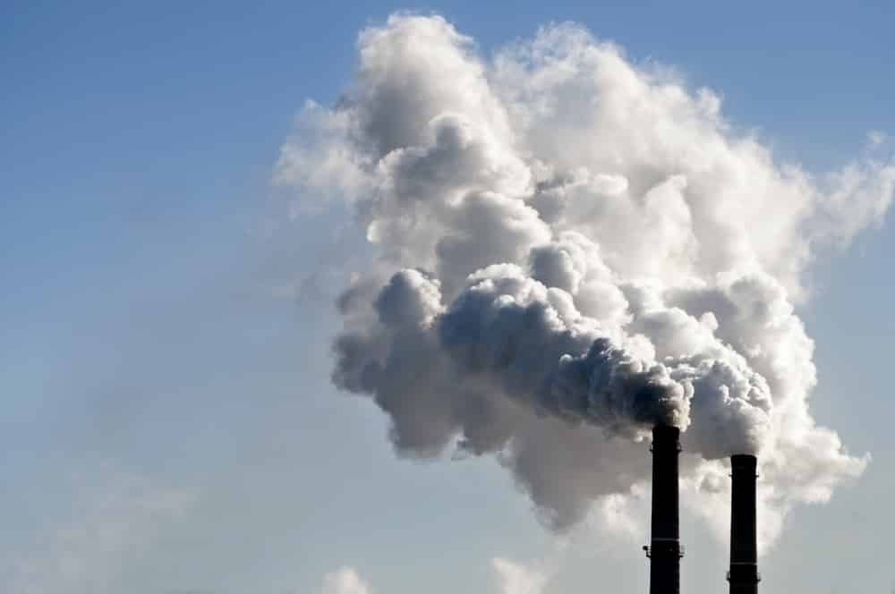 Close-up of factory chimneys emitting pollution into blue sky